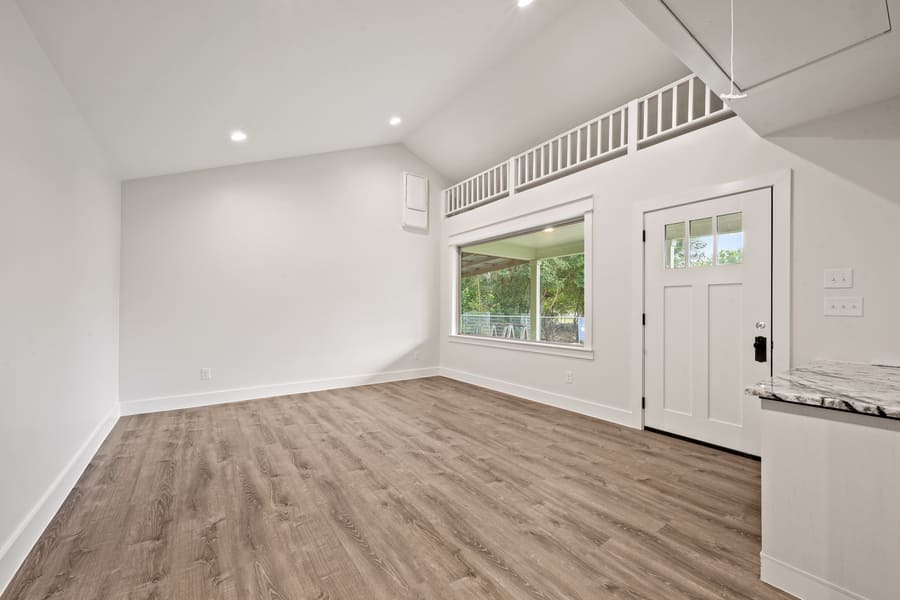 Empty room with wood flooring, white walls, a large window, and a white front door with glass panels.