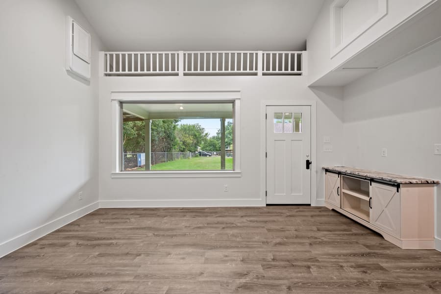 Empty modern room with light wood flooring, large window overlooking a green yard, white walls, a white door, and a built-in cabinet with a marble countertop.