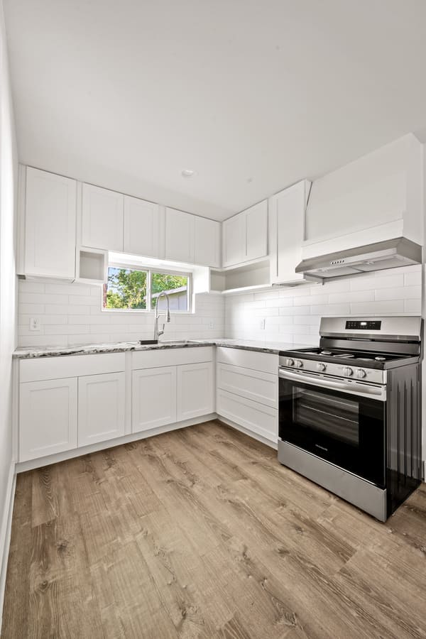 Modern kitchen with white cabinets, marble countertops, stainless steel oven, and wood-look flooring.