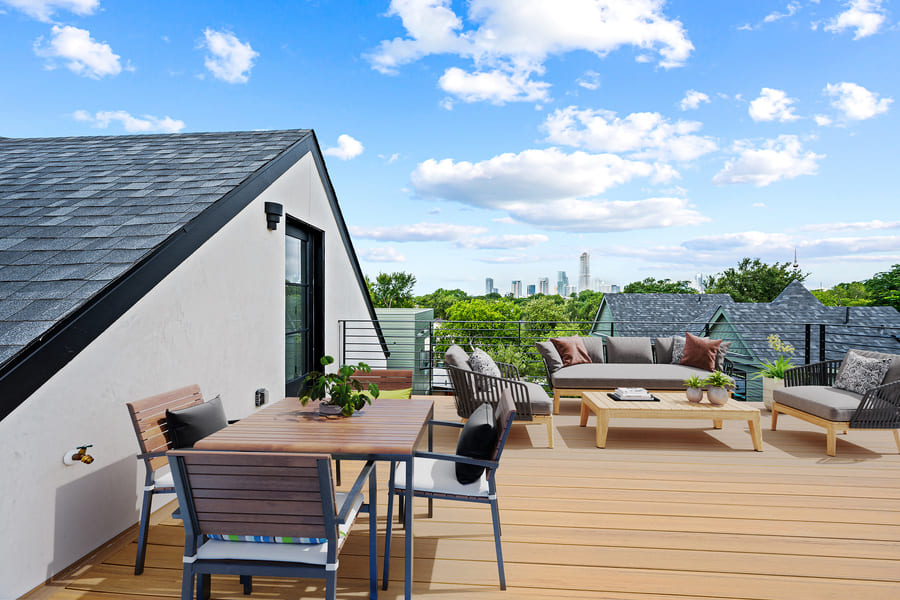 Modern open-plan living space with white marble dining table, beige chairs, a brown sofa, wall-mounted TV, and kitchen with wooden and white cabinetry.